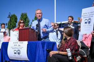 A man in a blue shirt and tie speaks to a crowd holding campaign signs