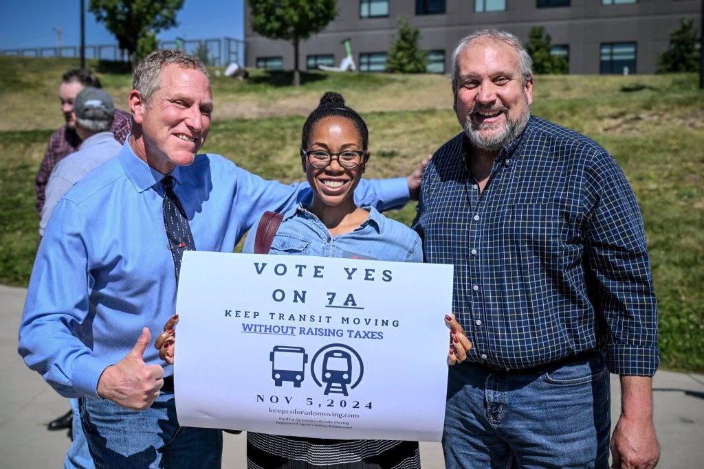 Three people hold up a sign that reads Vote Yes on 7A