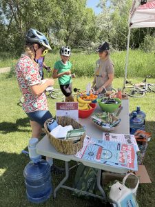 Three people in bicycle gear stand around a table filled with giveaways during the B360 bicycle ride