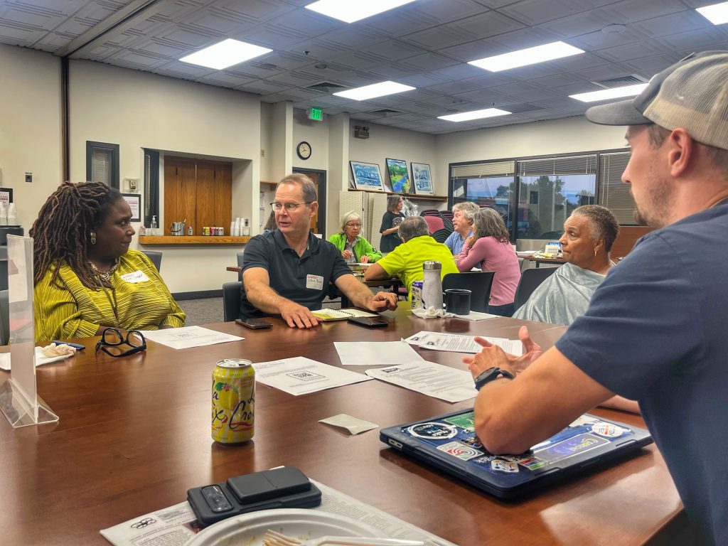 A diverse group of people sits around a table talking during a community event at the Boulder Chamber.