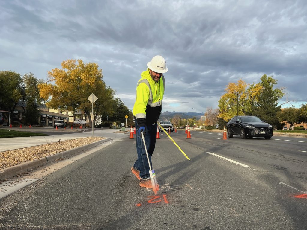 A construction worker uses a tool to paint temporary markings on the pavement on Arapahoe Avenue in Boulder