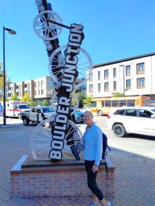 A woman wearing a blue long-sleeved top stands in front of the Boulder Junction wayfinding sign.
