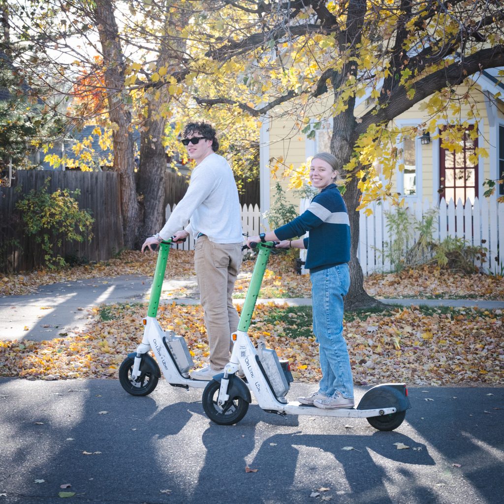 Two people ride Lime e-scooters on a street in Boulder