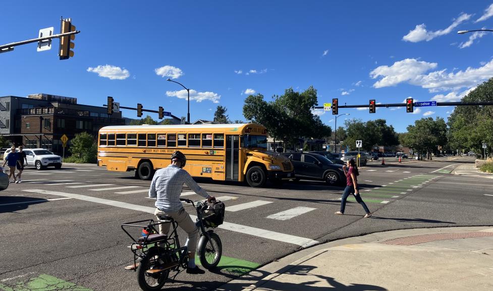 A photo showing the intersection of Folsom Street and Arapahoe Avenue, showing a bicyclist, a pedestrian, and a school bus at the intersection.